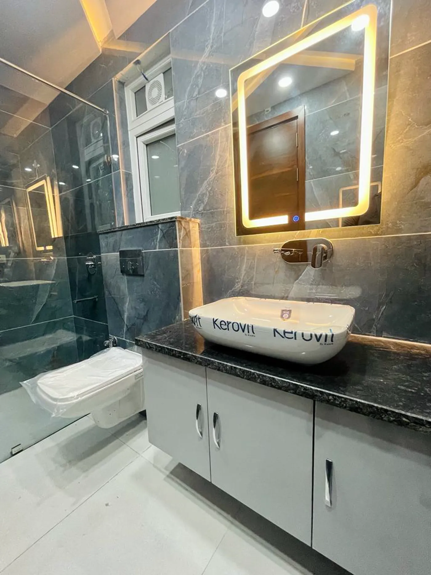 Bathroom with dark stone vanity, white vessel basin and backlit mirror