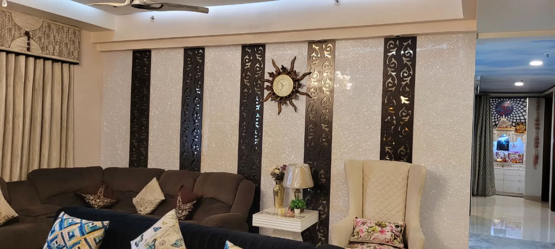 Living room with sculptural gold and mirrored mosaic feature wall, brown recliner sofas and crystal chandelier